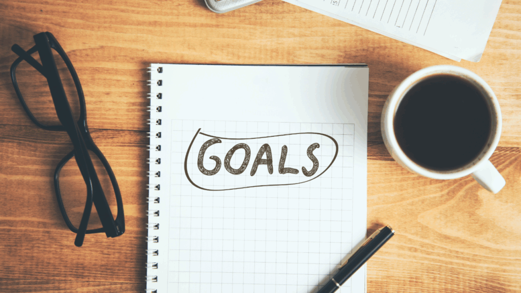 Adobe Stock - Goals written on Notepad next to a cup of coffee and glasses